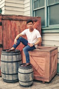 Full length portrait of young man sitting by barrels