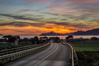 Vehicles on road against dramatic sky during sunset