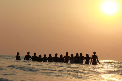 Silhouette people on sea against clear sky during sunset