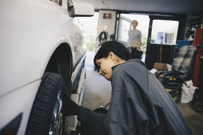 Female mechanic examining car wheel at auto repair shop