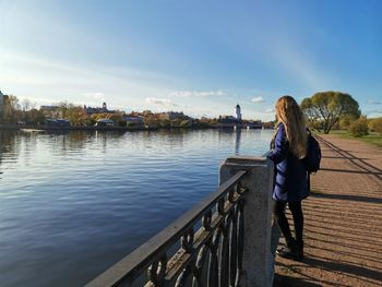 Woman sitting on railing by river against sky