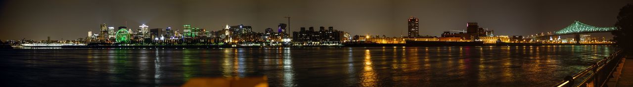 Illuminated buildings by river against sky at night