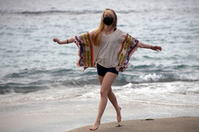 Portrait of young woman with arms outstretched walking at beach