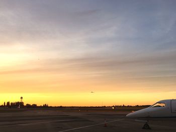Airplane on runway against sky during sunset