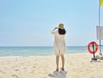 Rear view of woman standing on sand at beach against clear sky