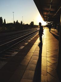 Silhouette woman standing on railroad station platform against sky