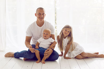 Father with daughter and son sitting on a white wooden floor in a large room
