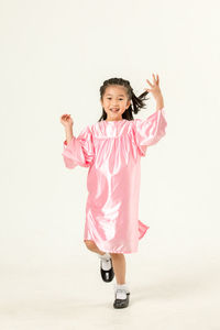 Full length of girl in pink graduation gown against white background