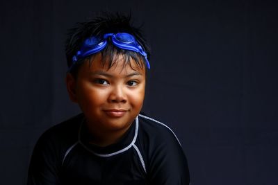 Portrait of boy wearing swimming goggles against black background