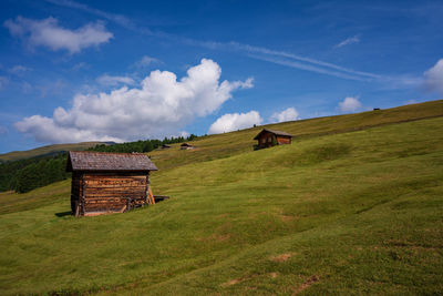 Log cabins on green hill against cloudy sky