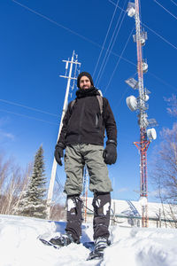 Man standing on snow covered field against blue sky