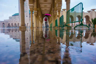 Girl with umbrella standing under arches in hassan ii mosque in casablanca, morocco 