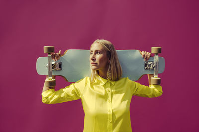 Portrait of young woman looking away against pink background