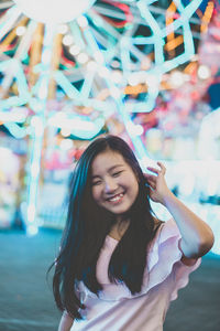 Smiling young woman standing at amusement park during night