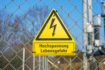 Close-up of high voltage sign on chainlink fence