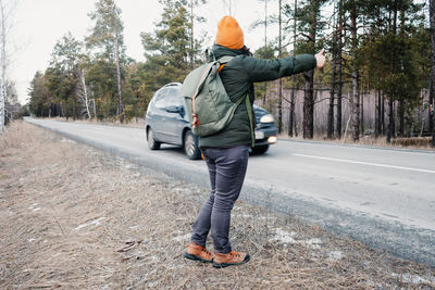 Middle-aged woman with backpack hiking in road and trying to stop car, hitchhiking solo tourism
