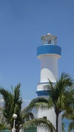 Blue and white colored lighthouse by sea against clear sky