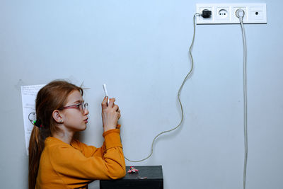 Portrait of woman holding camera against wall