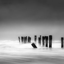 Wooden posts in sea against sky