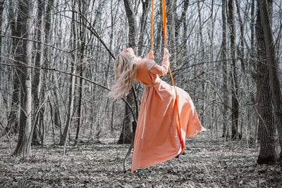 Woman swinging in swing by tree trunk in forest