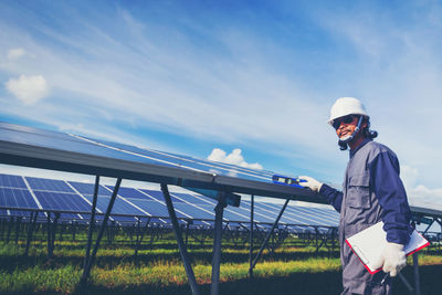 Male technician inspecting solar panels against sky