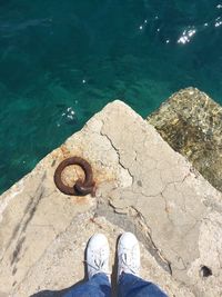 Low section of man standing on pier over sea during sunny day