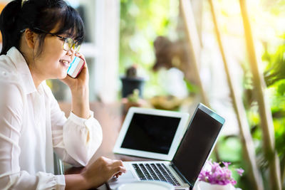 Rear view of woman using mobile phone at table