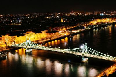 Illuminated bridge over river in city at night