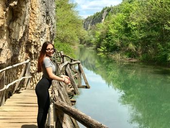 Young woman sitting by lake against trees