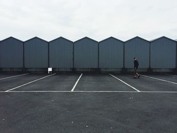 Side view of man walking in empty parking lot against sky