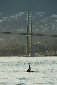 Man sitting on bridge over river against sky