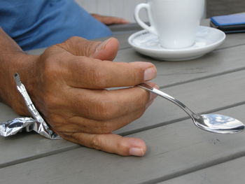 Cropped hand of man holding spoon on wooden table
