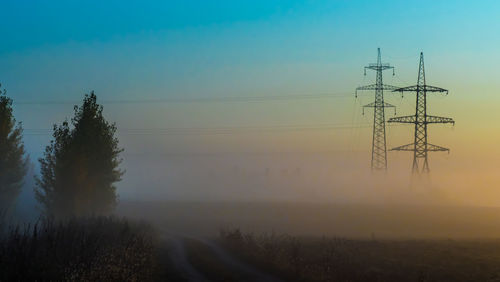 Electricity pylon on landscape against sky during foggy weather