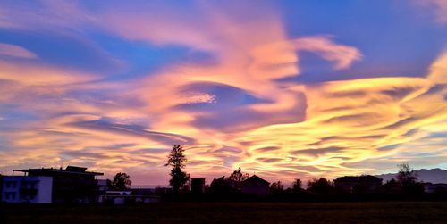 Silhouette houses against dramatic sky during sunset