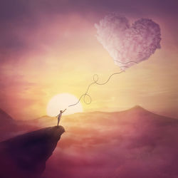 A person on the cliff and a heart shaped cloud like a kite raising up in the air. magical love scene