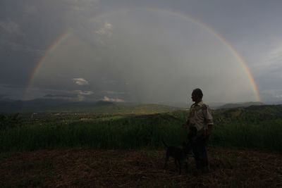 Man standing on field against rainbow in sky