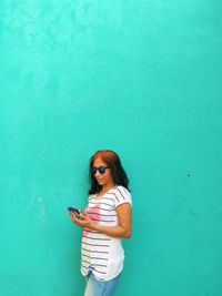 Woman using phone while standing against wall