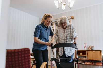 Female caregiver supporting senior woman using mobility walker at home