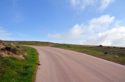 Empty road amidst field against sky