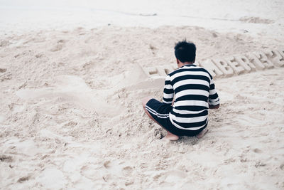 Rear view of boy sitting on sand at beach