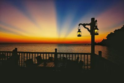 Silhouette railing by sea against sky during sunset