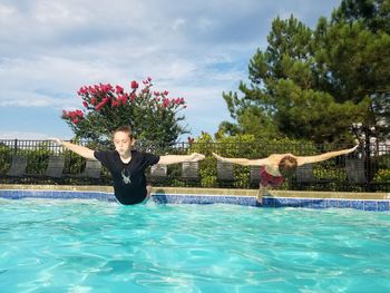 Boys with arms outstretched jumping in swimming pool