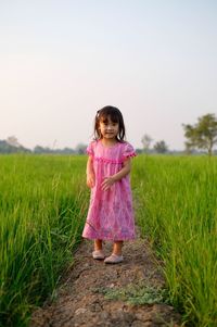 Portrait of girl standing at rice paddy against clear sky during sunset