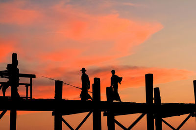 Silhouette people standing by railing against orange sky