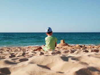 Rear view of boy on beach against clear sky