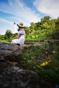 Side view of woman sitting on rock against sky