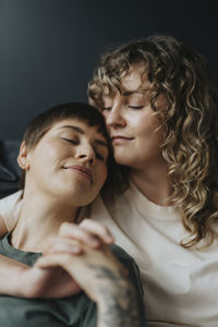 Lesbian woman with eyes closed leaning on girlfriend's shoulder while holding hands