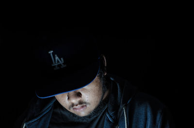 Close-up of man wearing cap against black background