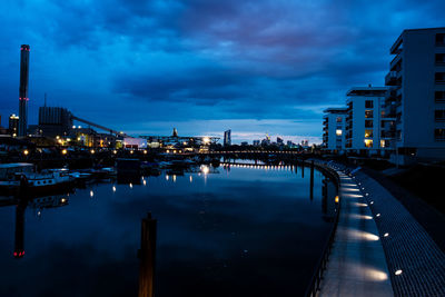 Illuminated city by river against sky at dusk