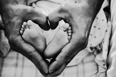 Cropped hands of man making heart shape with baby feet